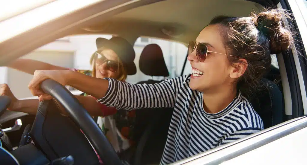 Zwei Freundinnen sitzen lachend auf den Vordersitzen im Auto