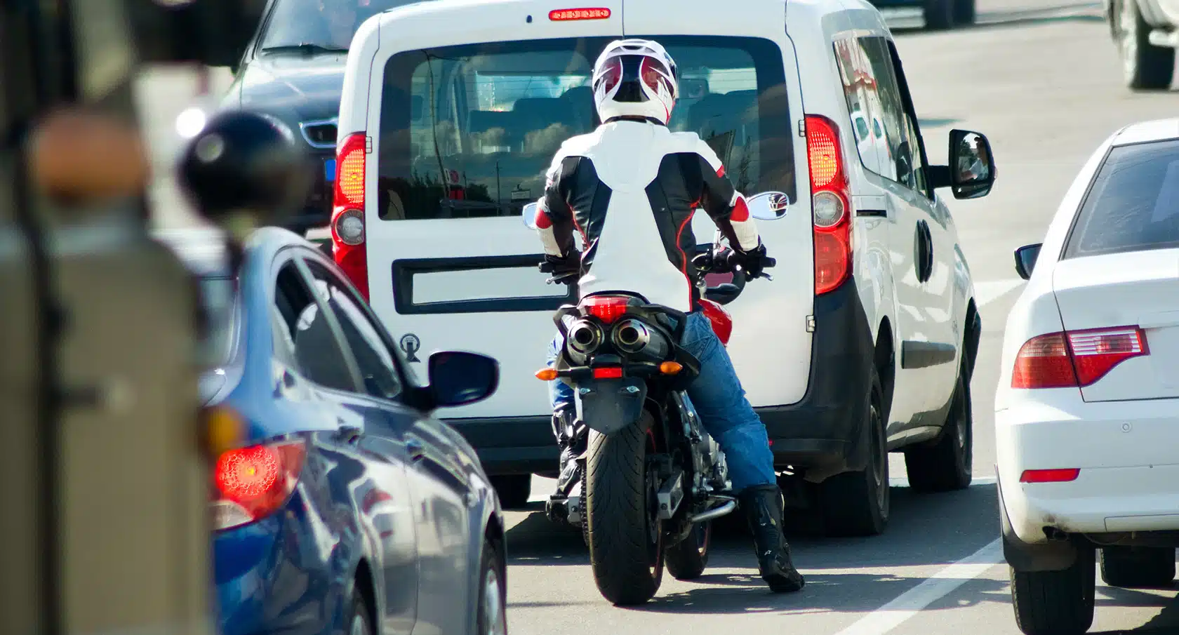 Motorradfahrer auf seiner Maschine steht hinter einem Auto im Stau